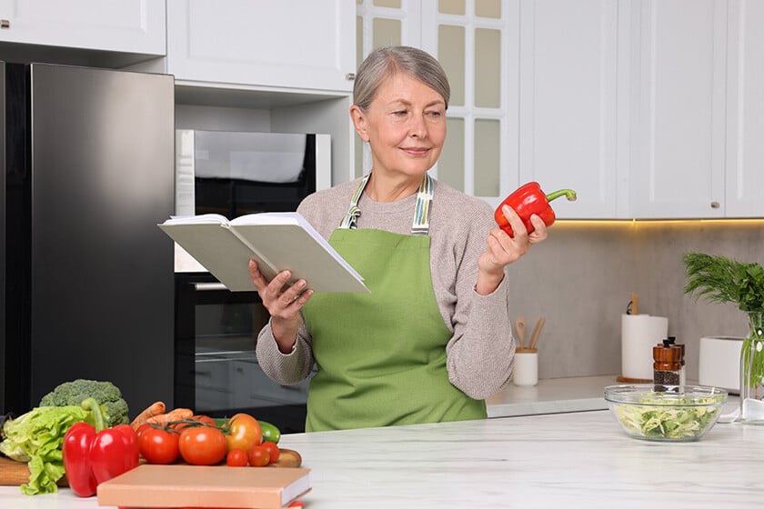Happy woman with recipe book and bell pepper in kitchen