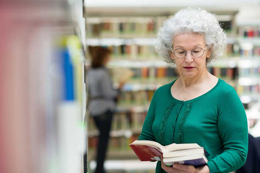 Senior woman reading and choosing book in library