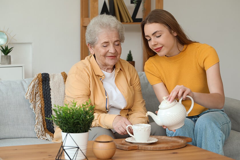 Young woman pouring tea into cup for her grandmother at home